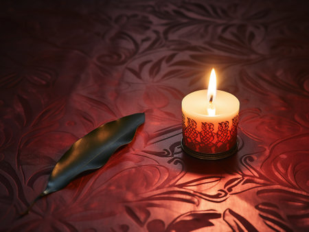 Burning candle on a red background with a leaf in the foregroundの写真素材