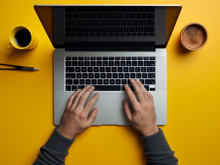 Person using a laptop computer with a cup of coffee on a yellow backgroundの写真素材