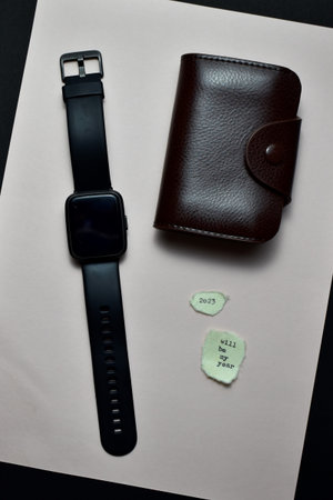 Black leather wallet and smart watch on white paper. Black background.