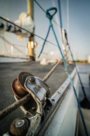 Detailed view of a sailboat's pulley system and rigging components, featuring a weathered rope and metal hardware against a blurred background of the boat's deck and mast. The nautical highlights setup functionality and craftsmanship.の写真素材