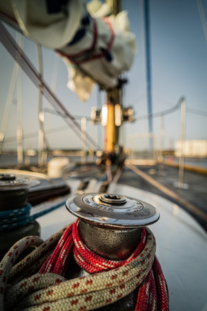 A detailed close-up of a sailboat winch wrapped with colorful ropes, highlighting essential sailing equipment. The blurred mast and rigging in the background emphasize the nautical setting and marine adventure.の写真素材