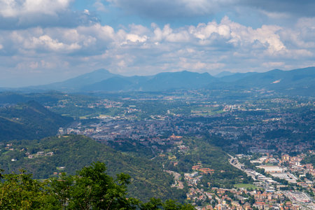 Aerial view of a valley town surrounded by rolling hills and mountains under a partly cloudy sky, showcasing urban areas, greenery, and distant peaks.の写真素材