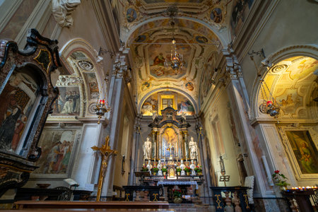 The ornate interior of a historic church featuring a decorated altar, religious paintings, frescoes, and intricate architectural details, illuminated by soft natural light and candlelight.の写真素材