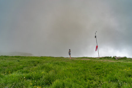 A person stands on a grassy hilltop near a windsock and weather station, surrounded by thick fog, creating a tranquil and atmospheric scene.の写真素材