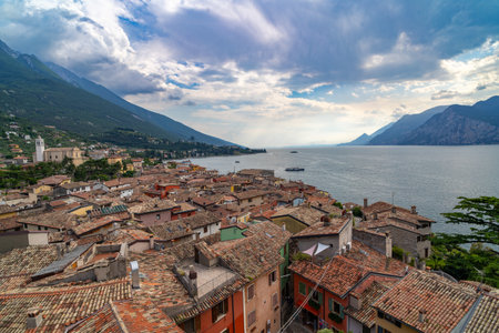 Picturesque view of a lakeside village with colorful tiled rooftops, nestled between mountains and calm waters under a partly cloudy sky.の写真素材