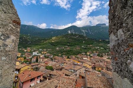 Charming hillside village with colorful houses and terracotta rooftops, surrounded by lush green mountains under a partly cloudy sky, framed by ancient stone walls.の写真素材