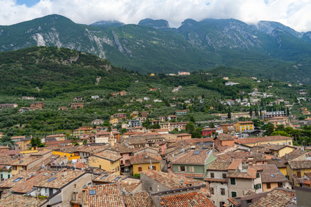 Colorful hillside village with terracotta rooftops, surrounded by lush greenery and towering mountains under a partly cloudy sky.の写真素材