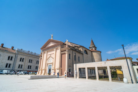 A historic church with classical architecture featuring statues and intricate details on its facade, situated in a spacious square with a modern colonnade structure.の写真素材