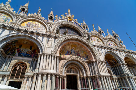 Facade of St. Mark's Basilica in Venice, Italy, showcasing intricate mosaics, arched entrances, and ornate sculptures against a clear blue sky.の写真素材