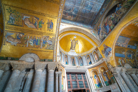 Golden mosaics and intricate frescoes adorn the interior of a historic basilica, showcasing religious art and marble columns under soft natural light.の写真素材