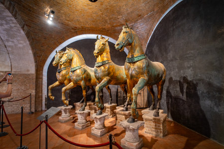Ancient bronze horse statues displayed in a museum exhibit, showing intricate craftsmanship and historical significance under warm lighting in a brick-arched room.の写真素材