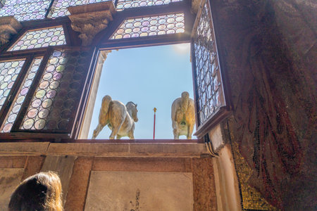 View of bronze horse statues through an ornate glass window with intricate patterns, capturing architectural elegance and historical art in daylight.の写真素材