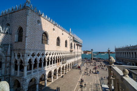 The Doge's Palace in Venice, Italy, showcases intricate Gothic architecture with arched windows and ornate details. Tourists gather along the waterfront with views of the lagoon.の写真素材