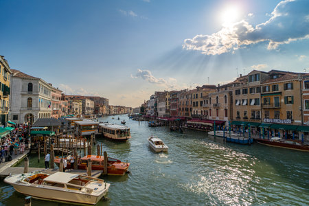Scenic view of Venice's Grand Canal with boats, gondolas, and waterfront buildings under a sunny sky. Tourists enjoy the lively atmosphere along the iconic waterway.の写真素材