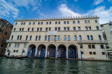 A historic building with arched entrances and ornate details along the Grand Canal in Venice, Italy. A gondola glides through the waters, showing Venetian charm and elegance.の写真素材