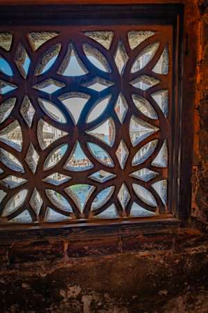 An intricate stone lattice window inside the Bridge of Sighs in Venice, Italy. The view reveals the canal below another bridge, offering a glimpse of Venice's iconic waterways and architecture.の写真素材
