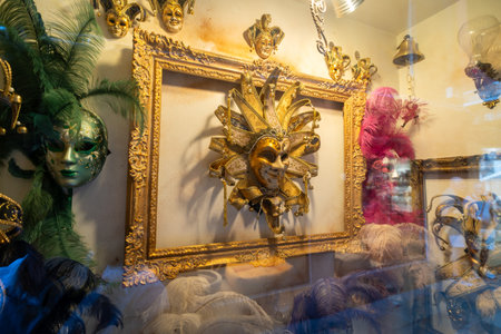 A vibrant display of Venetian carnival masks, featuring golden, green, and pink designs adorned with feathers and intricate details in a shop window.の写真素材