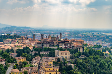 A picturesque aerial view of a historic Italian city with old buildings, bell towers, and lush greenery, extending to the horizon under a cloudy sky.の写真素材