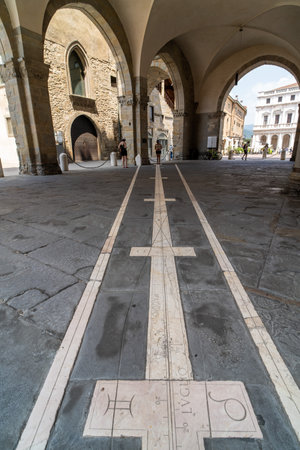 A detailed view of a historic stone sundial embedded in the ground, located under a beautifully arched portico in a charming Italian town.の写真素材