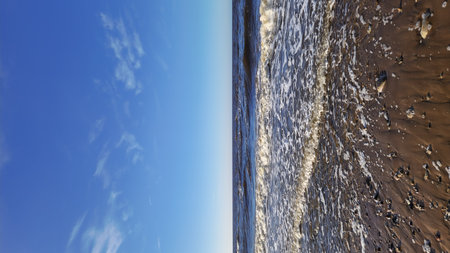 A vibrant scene of foamy waves washing over a sandy beach under a brilliant blue sky.の写真素材
