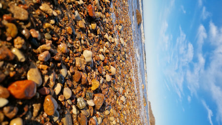 Wide-angle view of a vibrant beach with colorful pebbles in the foreground and dynamic waves under a clear blue sky.の写真素材