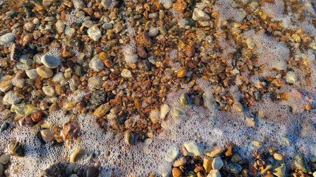 As dusk sets in, foamy seawater mixes with colorful beach pebbles, creating a dynamic and textured scene.の写真素材