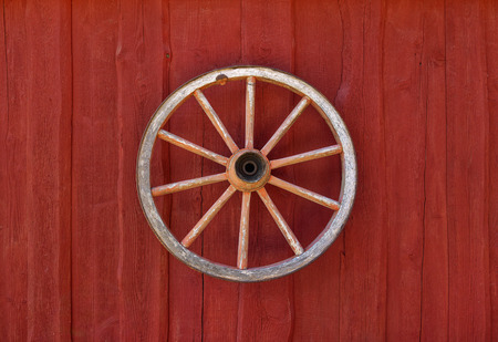 Old clean cartwheel hanging on red wooden wall as rural decoration.の写真素材