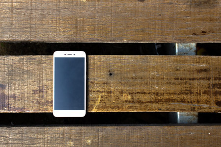 White smart phone with isolated screen on old wooden desk.  Top view with copy spaceの写真素材