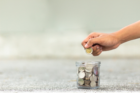 hand drops money into a glass jar for a savingsの写真素材