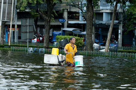 BANGKOK, THAILAND - OCTOBER 28: man leading his bike navigating through the flood on pra pin klow...