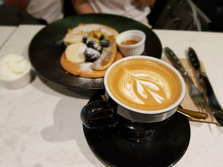Freshly make pancake topped with slice of banana, barries, honey syrup and butter. Cup of latte with beatiful latte artの写真素材