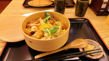 A bowl of Japanese chicken rice with a raw egg on top. Local fresh farm chicken. Garnish with some coriander, slices of radish pickle and a cup of hot green tea. Refreshing. Tokyo, Japanの写真素材