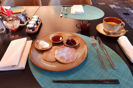 Pancake breakfast with a dash of icing sugar, flavour with cream cheese, honey and berries. And a cup of fresh hot coffee. Perfect table arrangement with dining napkin. Hot towel to wipe hands before diningの写真素材