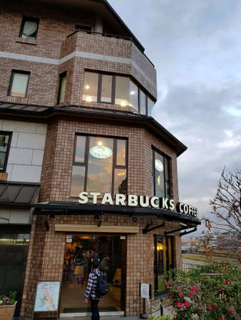 Starbucks Coffee at Sanjo Dori next to the Sanjo Bridge. People queueing inside the shop to buy food and drink. Grey blue sky in the evening. Kyoto, Japan.のeditorial素材
