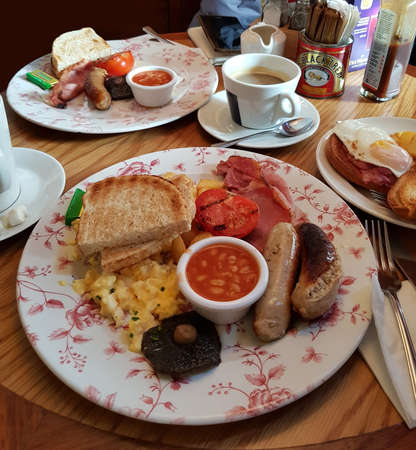 Traditional common full breakfast includes bacon, sausage, egg, baked bean, tomato, mushroom, toast and a cup of coffee. London, England, United Kingdom.の写真素材