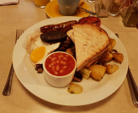 A full English breakfast includes bacon, sausage, egg, black pudding, baked bean, tomato, mushroom, toast bread and a cup of coffee. London, England, United Kingdom.の写真素材
