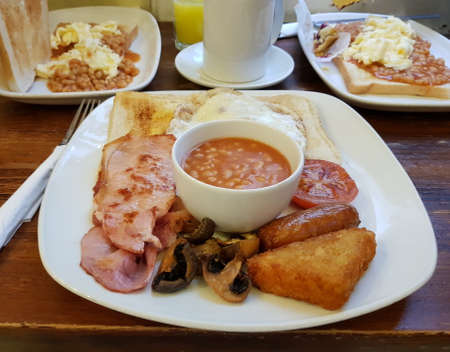 Traditional English breakfast with bacon, sausage, egg, baked bean, tomato, mushroom, toast bread and a cup of coffee. London, England, United Kingdom.の写真素材