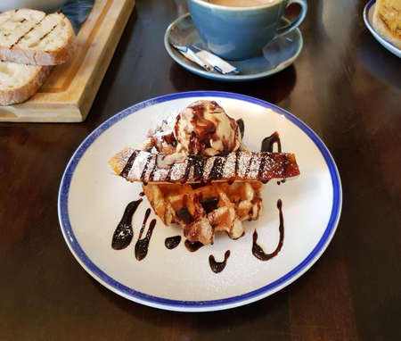 Afternoon coffee break with Belgian waffle and a scoop of vanilla ice cream. Chocolate and icing sugar on top. London, England, United Kingdom.の写真素材