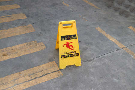 Yellow plastic sign with red symbol of slip and black text of caution wet floor on the floor. the sign of care taken to avoid danger or mistakes.の写真素材