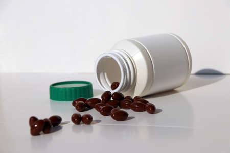 Pile of dark brown medicine on the white floor and white plastic bottle with green cap.の写真素材