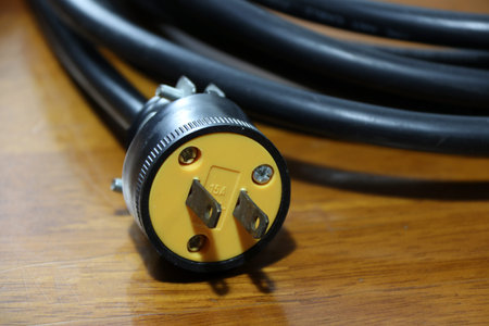 Yellow plug with black cable on the wooden floor. Used for electrical connection. Long distance...