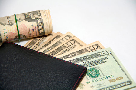 Black wallet with US money and roll banknotes use a rubber band on white background, US dollar...