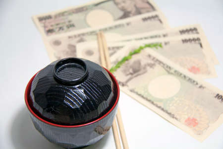 Black color red edge Miso soup bowl and wooden Chopsticks with Yen banknotes of Japan on the white background. The concept of Eat well live happily by Japanese style.の写真素材