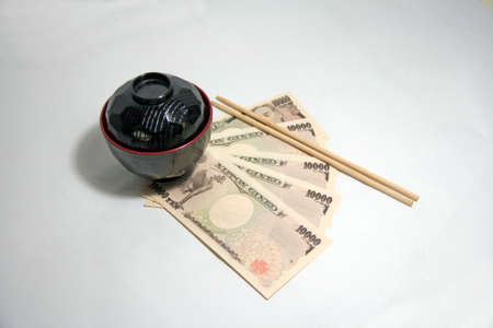 Black color red edge Miso soup bowl and wooden Chopsticks with Yen banknotes of Japan on the white background. The concept of Eat well live happily by Japanese style.の写真素材