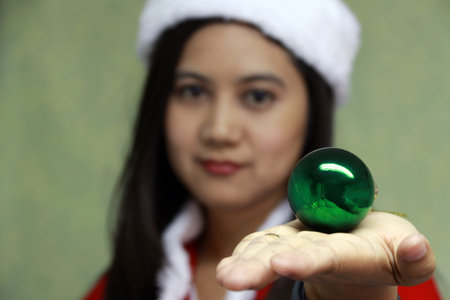Green magic ball on the hand of out focus Asian Santa Girl Dress. Woman in white and red Santa Dress with green ball in hand.の写真素材