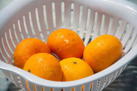 Five orange fruit in a white plastic basket. Orange is a round juicy citrus fruit with a tough bright reddish-yellow rind.の写真素材