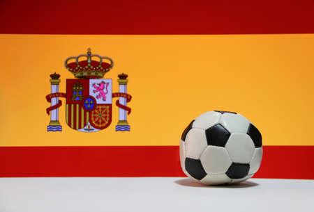 Small football on the white floor and Spanish nation flag background. The concept of sport, Spain is one of the finalists in football tournament of the world.の写真素材
