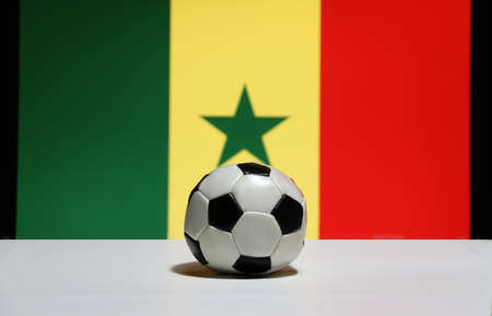 Small football on the white floor and Senegalese nation flag background in green, yellow and red color. The concept of sport.の写真素材