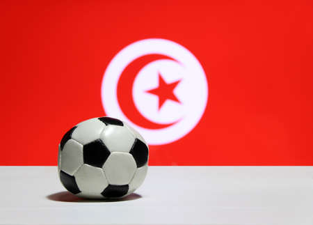 Small football on the white floor and Tunisian nation flag with moon and star background. The concept of sport.の写真素材