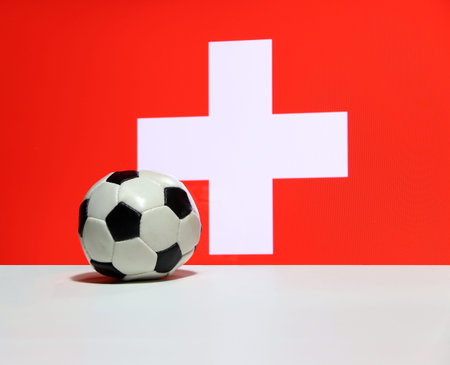 Small football on the white floor with white cross on red color of Swiss nation flag background. The...